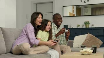 Multi ethnic family of three playing a video game at home sitting on the couch.