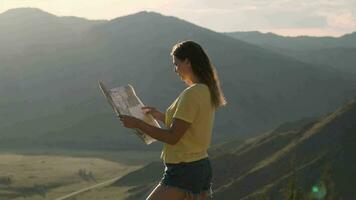 bellissimo ragazza turista guardare un' carta geografica mentre in piedi su il bordo di un' montagna durante tramonto video