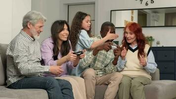 Happy multiethnic family of different age generations playing video game at home sitting on the couch.