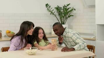 Cheerful family of different races play board game at home. The daughter removes wooden blocks from the tower and laughs. video