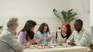 multi étnico familia de diferente años generaciones jugar tablero juego a hogar sentado a el mesa. el niño lanza el dado en el mesa y gana video