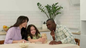 Happy family of different races play board game at home. The daughter removes wooden blocks from the tower and laughs. video