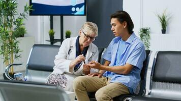 Elderly medic measuring glucose level using glucometer instrument, doing health examination with diabetic patient during checkup visit appointment in hospital waiting room. Medicine concept photo