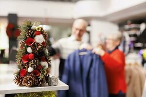 Selective focus of clients on videocall, showing clothes on online call during christmas shopping spree. Senior couple looking for clothing items in fashion boutique, seasonal sales at mall. photo