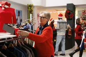 Client checking accessories box in clothing store, searching for ties and belts to give presents on christmas eve celebration. Elderly woman browsing through clothes on hangers, winter promotions. photo