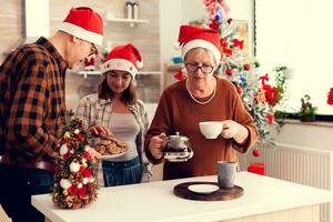 contento niño vistiendo Papa Noel sombrero comiendo delicioso galletas desde abuelo mientras celebrando invierno Días festivos con ellos foto