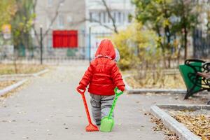 A small kid with a rake and a shovel walks in the park photo