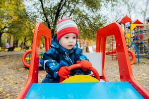 bebé sentado a el rueda de un para niños coche en el patio de recreo foto