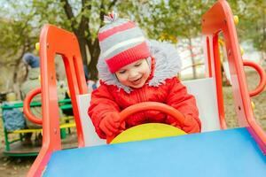 bebé sentado a el rueda de un para niños coche en el patio de recreo foto