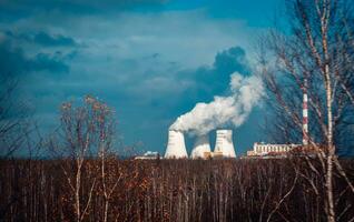 Nuclear power plant cooling towers concept photo. Big chimneys. Forest with partly cloudy sky in Polish province. photo