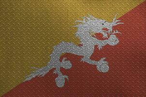 Bhutan flag depicted in paint colors on old brushed metal plate or wall closeup. Textured banner on rough background photo
