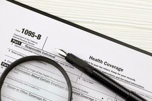 IRS Form 1095-B Health Coverage tax blank on A4 tablet lies on office table with pen and magnifying glass photo