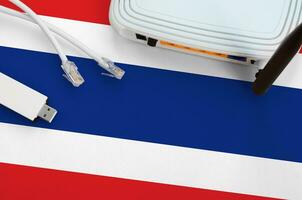 Thailand flag depicted on table with internet rj45 cable, wireless usb wifi adapter and router. Internet connection concept photo