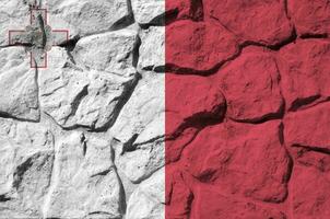 Malta flag depicted in paint colors on old stone wall closeup. Textured banner on rock wall background photo