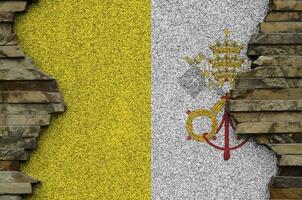 Vatican City State flag depicted in paint colors on old stone wall closeup. Textured banner on rock wall background photo