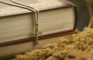 Silver necklace with crucifix cross on christian holy bible book on black wooden table. Asking blessings from God with the power of holiness photo