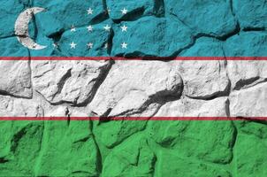 Uzbekistan flag depicted in paint colors on old stone wall closeup. Textured banner on rock wall background photo