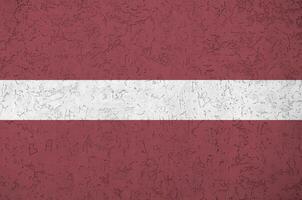 Latvia flag depicted in bright paint colors on old relief plastering wall. Textured banner on rough background photo