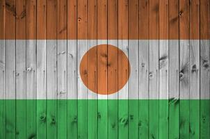 Niger flag depicted in bright paint colors on old wooden wall. Textured banner on rough background photo