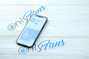 KHARKOV, UKRAINE - MARCH 5, 2021 Onlyfans icon and application on display screen on white table photo