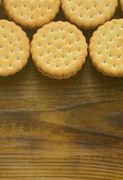 A round sandwich cookie with coconut filling lies in large quantities on a brown wooden surface. Photo of edible treats on a wooden background with copy space