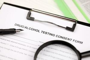 Drug and alcohol testing consent form on A4 tablet lies on office table with pen and magnifying glass photo