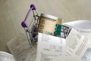 Indian rupees money bills bunch in shopping trolley surrounded by many paper receipts photo