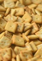 A lot of small cookies are square shaped. A pattern of a yellow salt cracker. Background image with salted pastry photo