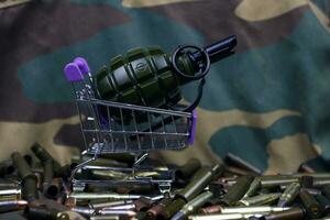 Rifle cartridges in small shopping cart. Big caliber ammo cartridges and hand grenades with a small shopping basket photo