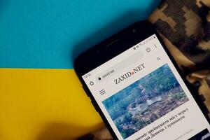 KYIV, UKRAINE - 4 MAY, 2023 Zaxid Net ukrainian news portal on smartphone screen with ukrainian flag and camouflage fabric photo