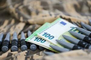 Bundles of euro bills and a machine gun belt on the camouflage uniform of a Ukrainian soldier. Concept of war financing, bribe or donation photo