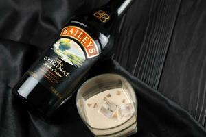 KYIV, UKRAINE - MAY 4, 2022 Baileys original alcohol bottle on wooden table with black fabric photo