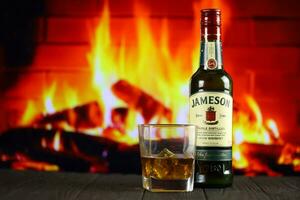 KYIV, UKRAINE - MAY 4, 2022 Jameson original alcohol bottle on wooden table with red fireplace photo