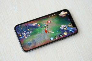 Honor of Kings mobile iOS game on iPhone 15 smartphone screen on wooden table during mobile gameplay photo