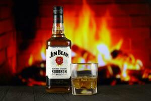 KYIV, UKRAINE - MAY 4, 2022 Jim Beam original alcohol bottle on wooden table with red fireplace photo