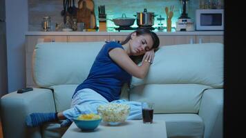 Woman sleeping on a sofa in front of TV while watching a bored movie. Tired exhausted lonely sleepy lady in pajamas falling asleep sitting on cozy couch in living room, closing eyes at night photo