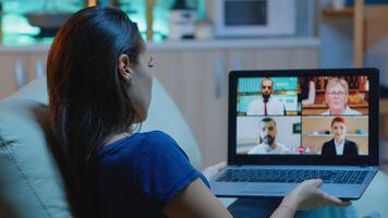 Woman in pijamas lying on sofa using laptop talking about sale report in video conference with team. Remote worker having online meeting consulting with colleagues using videocall and webcam chat photo