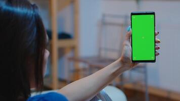 Housewife holding smartphone with chroma screen on hand looking at mockup. Reading on green screen template chroma key isolated mobile phone display using techology internet sitting on cozy couch photo