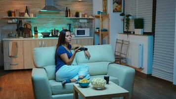 Young lady in pijamas watching Tv in living room sitting on sofa. Bored, home alone late at night woman relaxing watching tv lying on comfortable couch holding remote control changing TV channels. photo