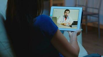 joven mujer hablando con médico en cámara web utilizando tableta foto