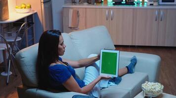 Woman holding touchpad with green screen sitting on sofa in living room. Housewife looking at template chroma key isolated smart notebook display using techology internet sitting on sofa. photo