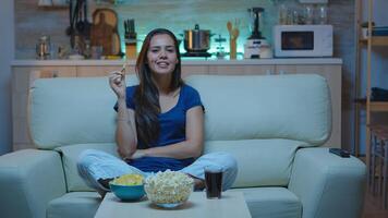 Lady talking on camera sitting on couch and eating snacks. Enthusiastic excitement alone woman looking at webcam discussing, socializing, networking with family using internet on skype in evening photo