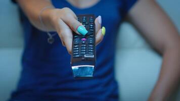 cerca arriba de mujer mano cambiando televisión canales sentado en sofá. televisión remoto controlar en el manos de dama señalando el televisión y elegir un película, participación controlador y prensado el botón foto