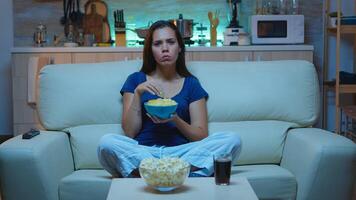 atento concentrado joven dama acecho película comiendo meriendas . conmocionado asombrado hogar solo a noche mujer con sorprendido cara mirando a suspenso película sentado en cómodo sofá. foto