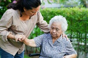 Caregiver help Asian elderly woman disability patient sitting on wheelchair in park, medical concept. photo