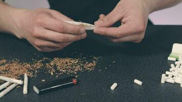 Man in Black Clothing is Rolling a Hand Made Cigarette Using Papers, Filters and Tobacco. A Way to Save on Tobacco Products. Tobacco Product Economy Concept. CloseUp Shot video