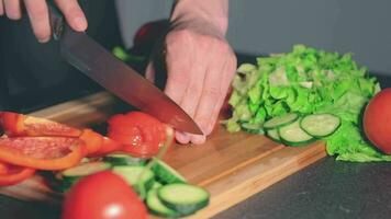 chef dans blach uniforme est Coupe des légumes à maison. cuisinier est en train de préparer Ingrédients pour quelque chose diététique. en bonne santé nourriture concept. dynamique fermer coup video