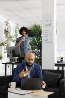 Arab entrepreneur presenting business plan to team during video conference call using laptop. Executive manager discussing product launch in videocall while sitting on couch in coworking space photo