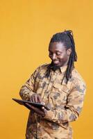 Cheerful young adult browing on internet using tablet computer in studio over yellow background. Smiling man scrolling trough social media, watching funny video on digital gadget photo