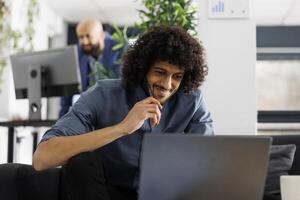 Smiling entrepreneur checking sales revenue growth on laptop while working in business office. Start up company entrepreneur analyzing marketing successful campaign in coworking space photo